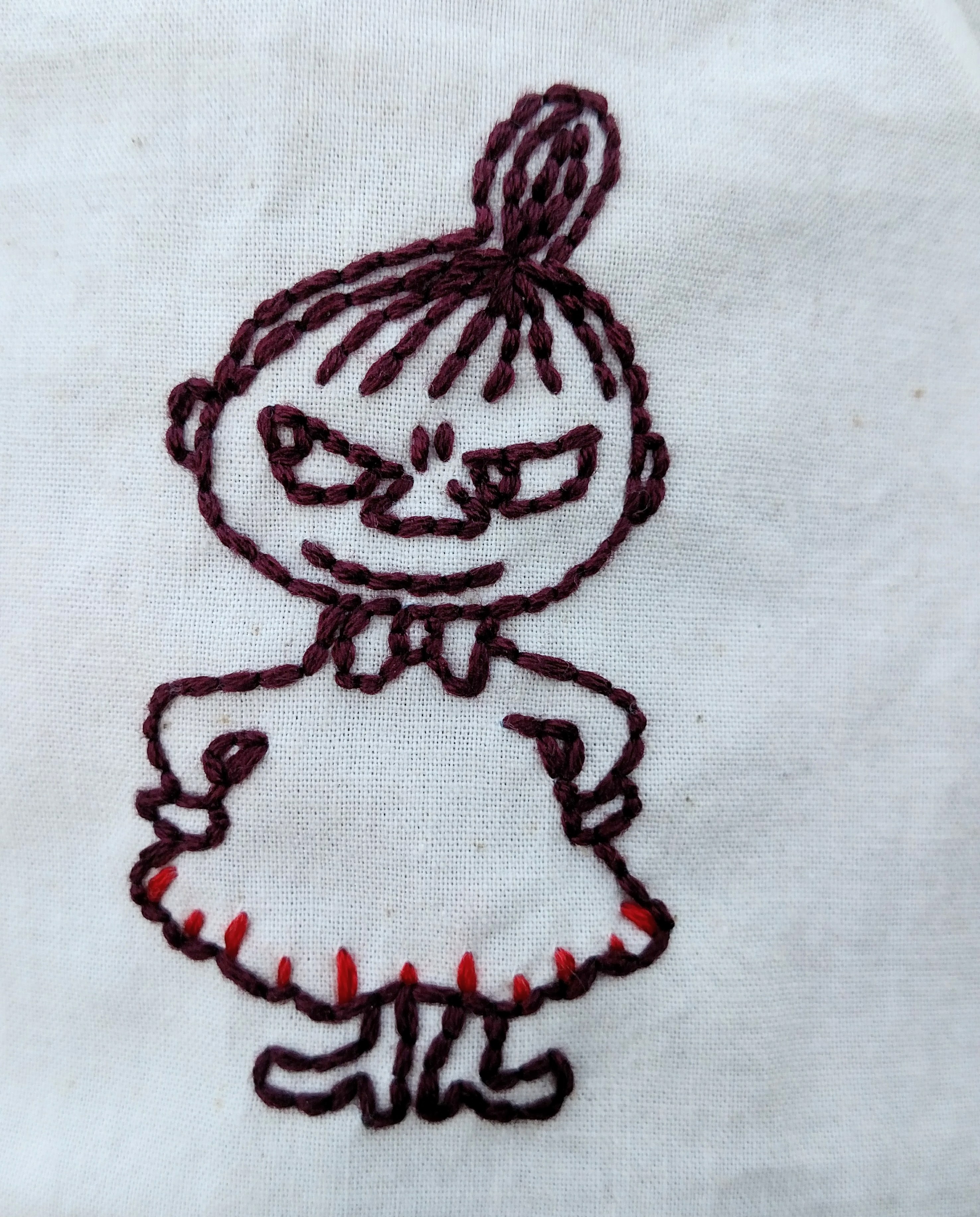 Little My has her hands on her hips and a devious little smirk on her face. She is embroidered in outline, and has little red stitches accentuating the hem of her dress.