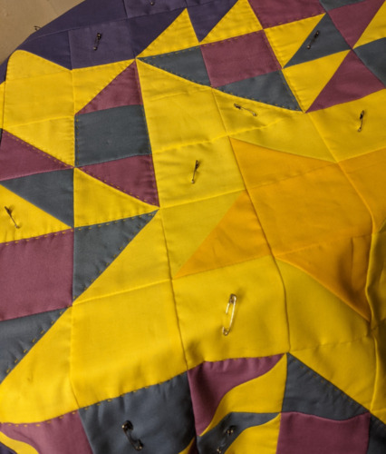 Unfinished quilt with big yellow stars. There are safety pins holding it together.